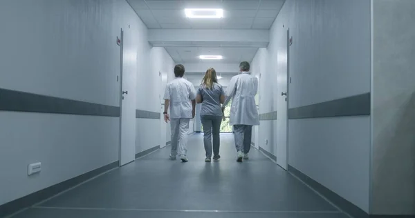 Following shot of doctors walking along the modern medical center corridor. Healthcare specialists and nurse enter the hospital room to patient or office. Medical staff in clinic hallway.