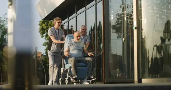 Dos Médicos Uniformados Llevan Anciano Con Discapacidad Entrada Clínica Silla —  Fotos de Stock