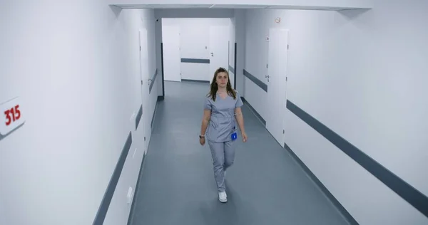 Bright hospital hallway: Doctors, professional medics, nurses, physicians and diverse patients walking. Medical personnel work in modern clinic or medical facility. Security camera view. High angle.