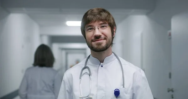 Mladý Doktor Brýlích Dívá Kameru Usmívá Profesionální Zdravotník Stojí Uprostřed — Stock fotografie