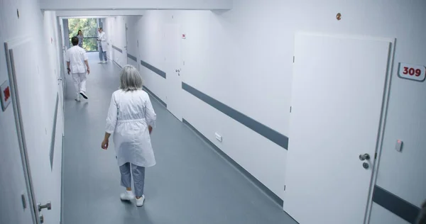 Bright clinic corridor: Busy doctors, professional medics, nurses, physicians and diverse patients walking. Medical staff work in modern hospital or medical center. Security camera view. High angle.