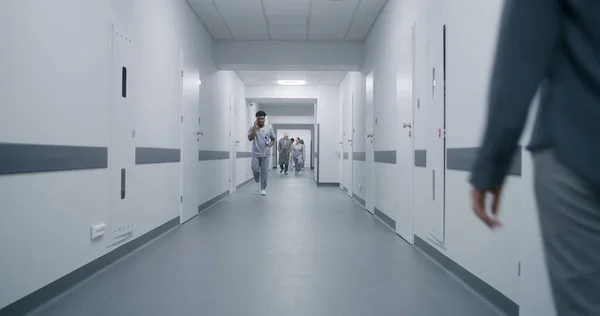 Woman goes medical center corridor, talks to African American doctor. Nurse and elderly patient walk clinic hallway, discuss tests results. Multiracial medical staff in clinic.