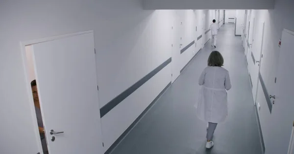 Clinic corridor: Busy doctors, professional medics, nurses, physicians and patients walking. Multiethnic medical staff work in modern hospital or medical center. Security camera view. High angle.
