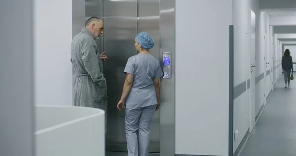 Üniformalı Hemşire Yaşlı Adamla Hastane Koridorunda Yürür Asansör Kapısına Gelir — Stok fotoğraf