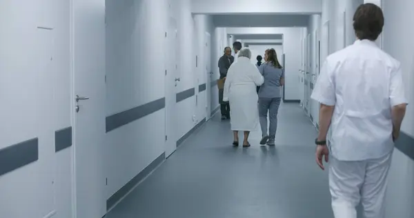 Dijital Tabletli Kadın Doktor Yaşlı Bir Kadınla Klinik Koridorunda Yürüyen — Stok fotoğraf