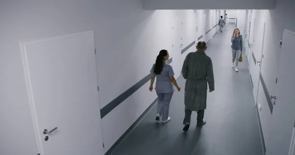 Clinic corridor: Busy doctors, professional medics, nurses, physicians and patients walking. Multiethnic medical staff work in modern hospital or medical center. Security camera view. High angle.