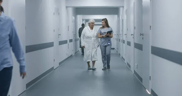 女性医師 デジタルタブレットコンピュータと高齢女性の話し合い 手術後に診療所の廊下を歩きます 医療スタッフ 医療センターホールの患者 — ストック写真