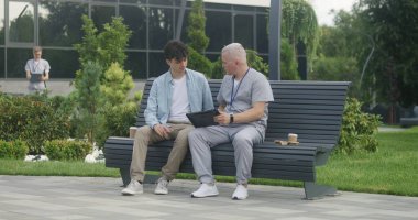 Elinde tabletle oturan doktor yetişkin bir hastayla bankta oturur ve ona tedavi önerir. Tıbbi üniformalı profesyonel, dijital tablet kullanan müşteriye teşhis koyuyor. Sağlık personeli dışarıda çalışıyor..