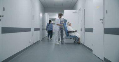 Profesyonel doktorlar yaşlı hastaları tekerlekli sandalyeyle sağlık odasına götürüp test sonuçlarını tartışırlar. Olgun doktor, meslektaşı ve kıdemli bayan için kapıyı açar. Tıbbi personel iş başında..