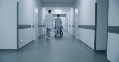 Hasta koridorda yürürken tekerlekli sandalyeyi iten doktorların arkası. Sıhhiyeciler konuşur, prosedürlere, terapiye ya da hastane odasına birini götürür. Tıbbi personel ve hastalar klinik koridorunda..