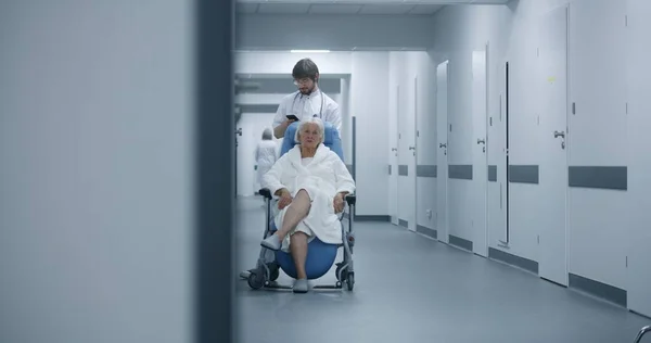 Erkek Doktor Klinik Koridorunda Tekerlekli Sandalyeli Yaşlı Bir Kadınla Duruyor — Stok fotoğraf