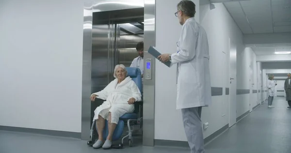 의사는 엘리베이터에서 환자를 휠체어로 이동시킵니다 의사는 수술을 받거나 진료소 복도를 — 스톡 사진