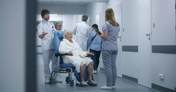 Krankenschwester Schiebt Rollstuhl Mit Patientin Klinikflur Ärztin Kommt Kollegin Und — Stockfoto