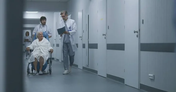 回廊に沿って歩いている患者と移動車椅子を押す医師の背景 医学の講演 セラピー または病院の部屋に人を連れて行ってください クリニックホールウェイの医療スタッフと患者 — ストック写真