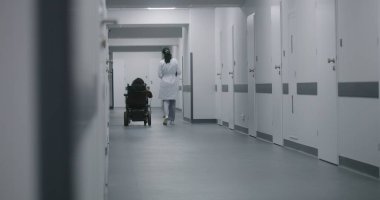 Kadın doktor klinik koridorunda yürüyor, fiziksel engelli bir kadına danışıyor. Doktorlar elektrikli sandalyedeki hastalara tıbbi prosedürlerden bahseder. Modern tıp merkezinin koridoru..