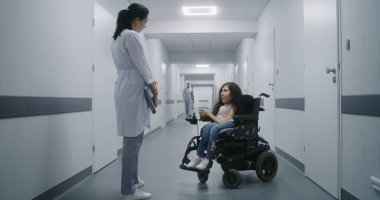 Hastane koridoru: Tekerlekli sandalyedeki SMA engelli kadın profesyonel doktorla sağlık kontrolü hakkında konuşuyor. Kadın hekim, modern klinik ya da tıp merkezinin parlak koridorunda hastaya danışmanlık yapıyor..