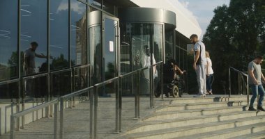 Fiziksel engelli bir kadın motorlu tekerlekli sandalyeyle kliniğe giriyor. Erkek hemşire kadın hastayla tanışıyor ve dönen kapılardan girilmesine yardım ediyor. Hastane ya da modern tıp merkezi dışında..