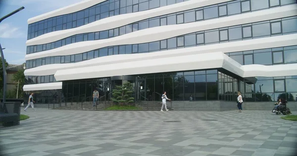 Courtyard of modern medical facility. Medical staff and diverse people enter and exit the hospital. Woman with physical disability rides to clinic on motorized wheelchair on appointment with doctor.