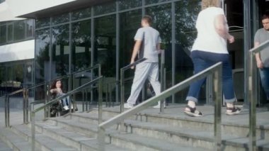Fiziksel engelli bir kadın motorlu tekerlekli sandalyeyle kliniğe giriyor. Sağlık çalışanı, erkek hemşire buluşur ve kadın hastaya içeri girmesinde yardım eder. Hastane ya da modern tıp merkezi dışında..