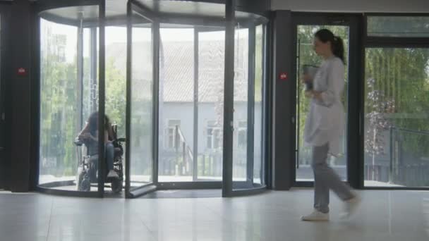 Kvinna Med Funktionshinder Åker Klinikens Entré Elektrisk Rullstol Genom Svängdörrar — Stockvideo