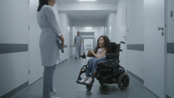 医院走廊 轮椅残疾妇女与专业医生谈论体格检查 女医生在现代诊所或医疗设施明亮的走廊咨询病人 — 图库视频影像