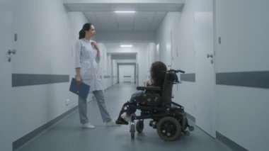 Kadın doktor klinik koridorunda duruyor. Tekerlekli sandalyede omurilik kası atrofisi olan bir kadına danışıyor. Doktor, engelli bir hastayla sağlık kontrolü hakkında konuşur. Modern tıp merkezinin koridoru..