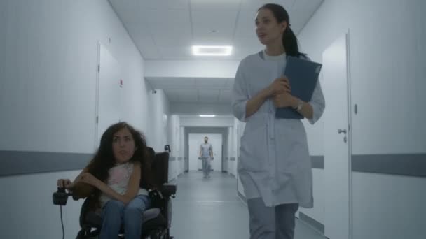 女医生走过诊所走廊 咨询残疾妇女 医生和坐在机动轮椅上的病人谈论医疗程序 医疗设施走廊 跟踪射击 — 图库视频影像