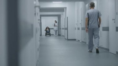 Kadın doktor klinik koridorunda yürüyor, fiziksel engelli bir hastaya danışıyor. Doktorlar motorlu tekerlekli sandalyedeki bir kadınla sağlık kontrolünden bahsediyorlar. Modern tıp merkezinin koridoru..