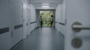 Genç Afrikalı Amerikalı çocuk hastane koridorunun sonunda arkadaşıyla birlikte pencerenin yanında duruyor. Kırık bacaklı beyaz bir genç başka bir ergenle klinik koridorunda konuşuyor. Sağlık merkezinde hasta var..