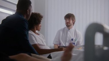 Doktor test sonuçlarını tablet bilgisayar kullanan hastalara bildiriyor. Afrikalı Amerikalı çocuk ve babası doktorla görüşüyor. Hasta ameliyattan sonra iyileşiyor. Hastane koğuşunda tıbbi personel.