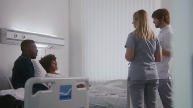 Yetişkin doktor ve hemşire hastane koğuşunda. Sıhhiyeci dijital tablet bilgisayarı tutuyor ve test sonuçlarını Afrikalı Amerikalı gençlere ve babasına açıklıyor. Hasta yatakta yatıyor, babasıyla ve doktoruyla konuşuyor..