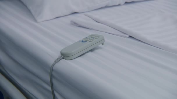 ホワイトシートに横たわるリモートコントロールの閉鎖 病院の部屋のベッドのライト ベッドの寝具 クリーンで明るい病院病棟は 患者に備えています 医療施設のモダンな設備と快適なベッド — ストック動画