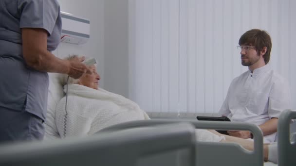 医生用平板电脑做检查 咨询在医院病房休息的老年女性病人 护士为成功手术后康复的老年妇女调整枕头和床 现代诊所 — 图库视频影像