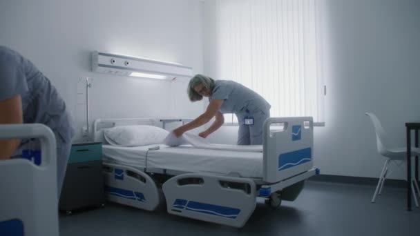 Dojrzała Sprzątaczka Dorosłym Kolegą Ścieli Łóżka Nowoczesnym Jasnym Oddziale Szpitalnym — Wideo stockowe