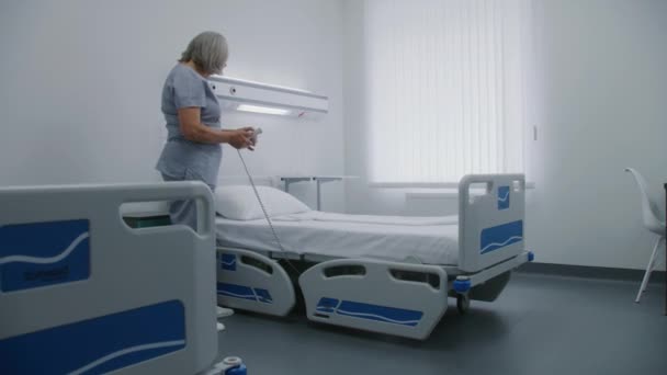 成熟的护士使用升降遥控器设置了智能舒适的床 女医务工作者为病人准备医院房间 诊所或医疗设施的现代化设备 Dolly Shot — 图库视频影像