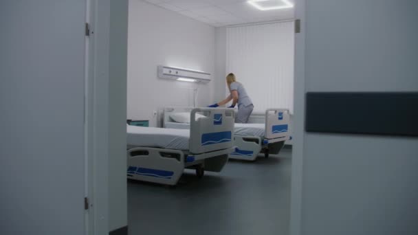 戴手套的成年护士在病房里用地毯擦拭床和病人床边面板 女清洁工清扫病房 为新病人准备好 在现代医疗中心工作的医务人员 — 图库视频影像
