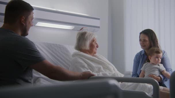 老年女性病人躺在明亮的病房的床上 与亲戚呆在一起 有爱心的家庭成员支持老年妇女在手术成功后康复 现代医疗设施或诊所 — 图库视频影像