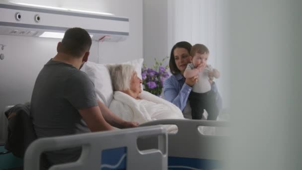 老年女性病人躺在明亮的病房的床上 与亲戚呆在一起 爱家探访成功手术后康复的外婆 现代医疗设施或诊所 慢动作 — 图库视频影像