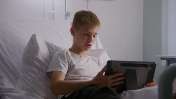 붕대가 다리를 소년은 침대에 태블릿을 사용하여 아버지와 이야기합니다 아이는 원격으로 — 비디오
