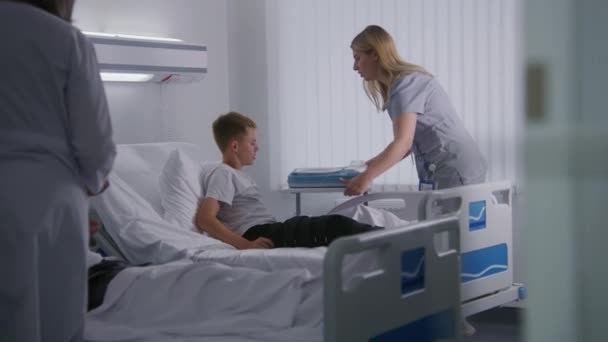 Sjuksköterska Ger Lunchlåda Till Vilande Ung Pojke Och Höjer Tillbaka — Stockvideo