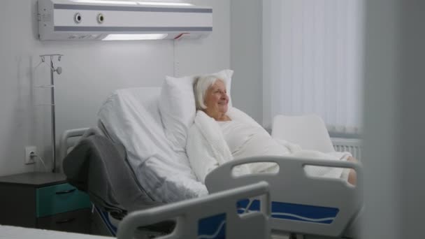 老年女性病人在明亮的病房卧床休息 爱家探访成功手术后康复的老奶奶 现代医疗设施或诊所 慢动作 — 图库视频影像