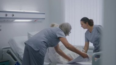 Hemşireler yaşlı kadın hastaların hastane koğuşunda yatmasına yardım eder. Tıp çalışanı yaşlı kadına uzaktan hemşire çağırma sistemini gösteriyor. Modern klinikte ya da tıbbi tesiste tıbbi personel. Yavaş çekim.