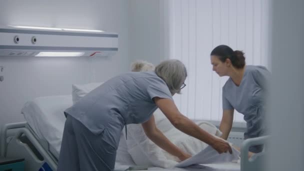 护士帮助老年女性病人躺在医院病房的床上 医务工作者向老年妇女展示远程护士呼叫系统 现代诊所或医疗设施的医务人员 慢动作 — 图库视频影像