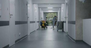 Tıp merkezi koridorunda paspas döşemesi. Çok kültürlü gençler pencerenin yanında durup konuşuyorlar. Kırık bacaklı beyaz çocuk arkadaşını terk edip klinik koridorunun sonundaki hastane koğuşuna gitmiş..