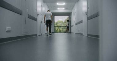 Yaralı beyaz, bacağı kırık bir genç hastane koridorundan hastane koridorunun sonundaki Afrikalı Amerikalı arkadaşına doğru yürüyor. Erkekler buluşur, el sıkışır ve pencerenin yanında konuşur..