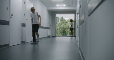 Yaralı beyaz, bacağı kırık bir genç hastane koridorundan hastane koridorunun sonundaki Afrikalı Amerikalı arkadaşına doğru yürüyor. Erkekler buluşur, el sıkışır ve pencerenin yanında konuşur..