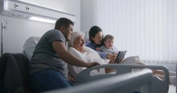 病院の部屋 愛する家族は 手術が成功した後に回復する高齢のおばあちゃんをサポートします デジタルタブレットを使用したビデオ通話による親戚の話 一緒に時間を過ごす 現代医療施設 クリニック — ストック写真