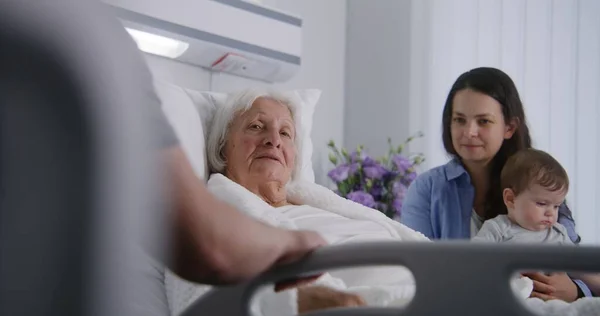 Starsza Kobieta Leży Odpoczywa Łóżku Jasnym Szpitalu Bawi Się Wnukiem — Zdjęcie stockowe