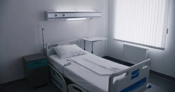Bright bedclothes on bed in hospital ward. Remote control lying on white sheets. Comfortable beds and modern equipment in medical facility. Light and clean hospital room ready for new patients.