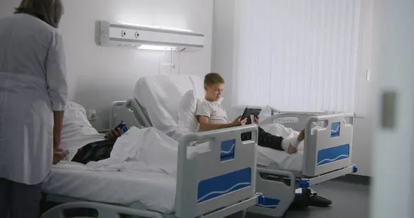 Bandajlı Bacağı Olan Genç Bir Çocuk Yatağa Uzanıyor Tablet Kullanarak — Stok fotoğraf